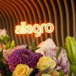 Flower arrangement in front of the neon Allegro sign at the Prague office opening