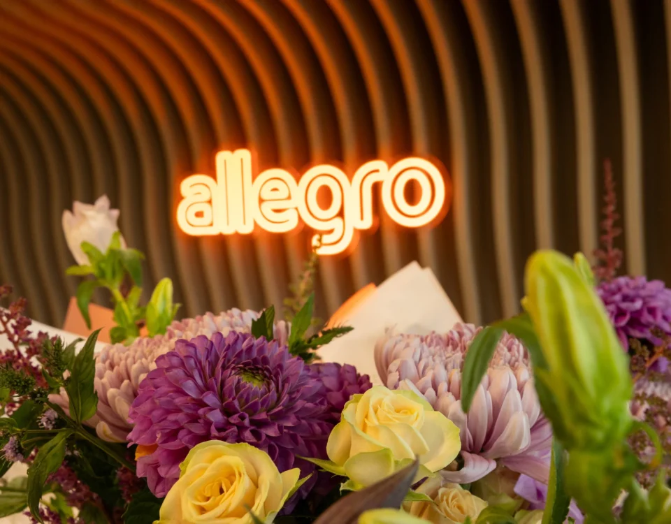 Flower arrangement in front of the neon Allegro sign at the Prague office opening