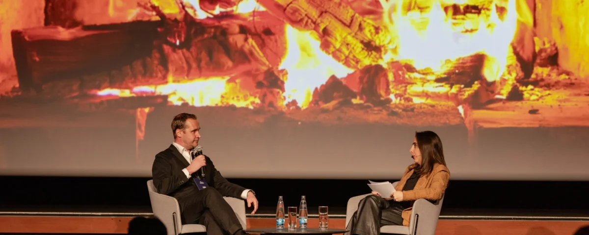 Fireside chat on stage in front of a fireplace projection at Hilton Prague Atrium
