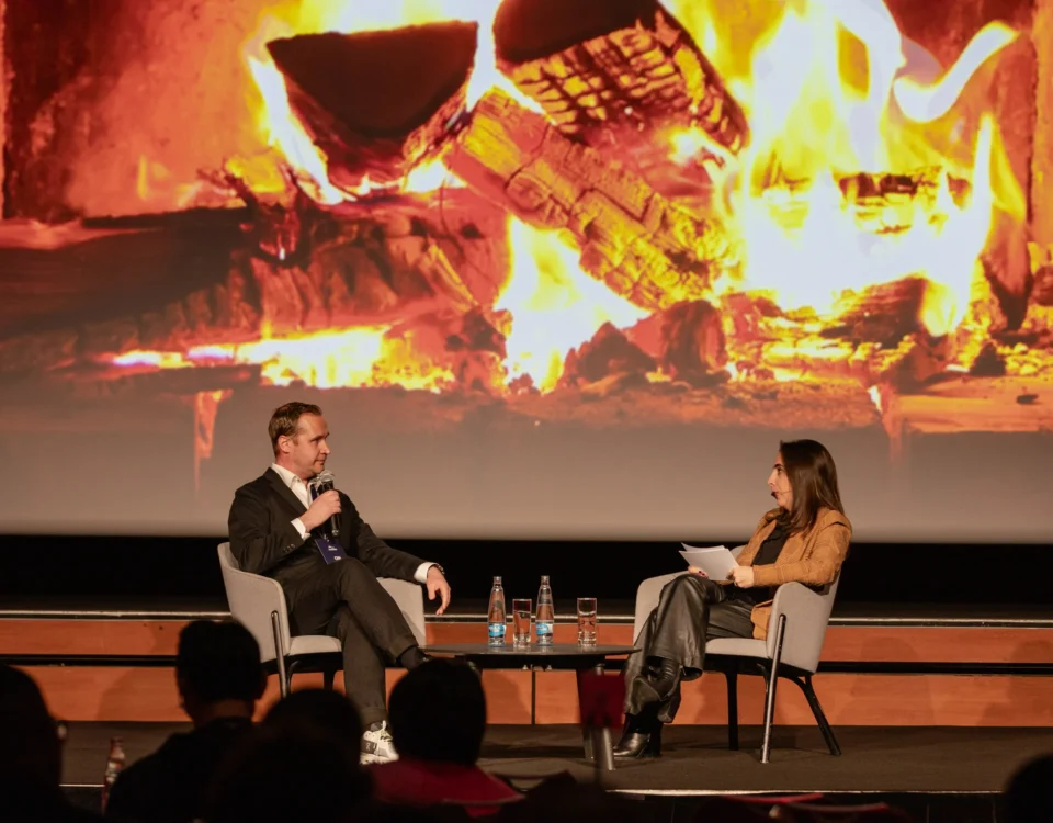 Fireside chat on stage in front of a fireplace projection at Hilton Prague Atrium